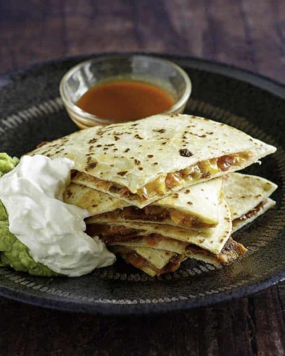 Cheese and bacon quesadilla cut into pieces served with sour cream, guacamole, and sour cream.