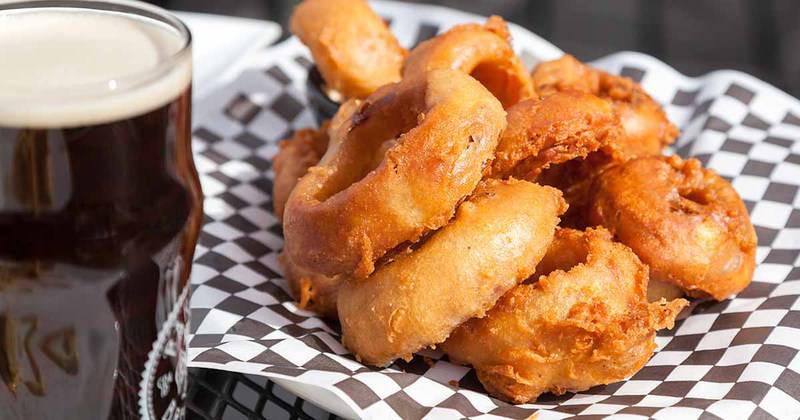 Homemade Simon and Seafort's onion rings on a plate and a beer next to it.