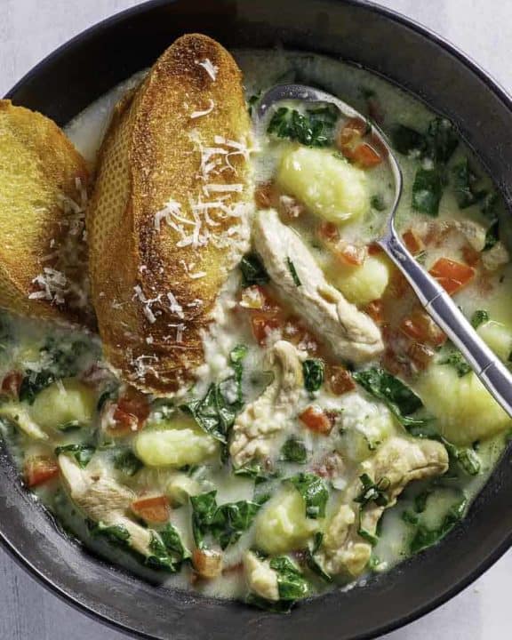 a bowl of homemade Macaroni Grill chicken Toscana soup and 2 pieces of toasted bread in it.