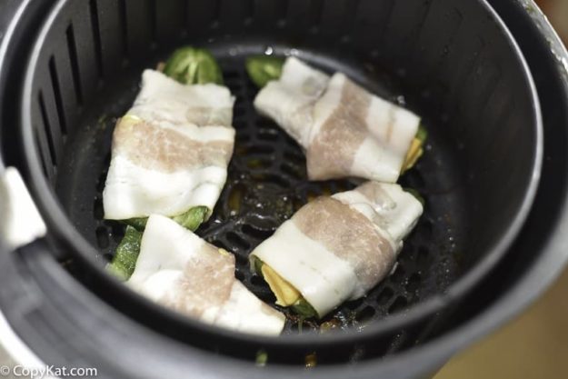 Bacon wrapped jalapeno poppers inside of an air fryer. 