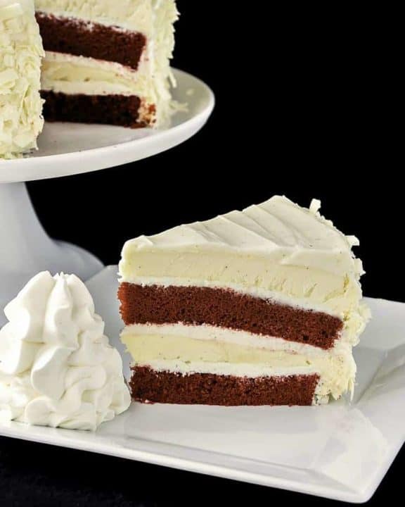a slice of homemade Cheesecake Factory Red Velvet Cheesecake beside the cheesecake on a stand.