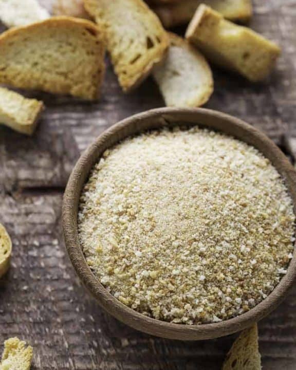 Homemade bread crumbs in a bowl next to pieces of bread.