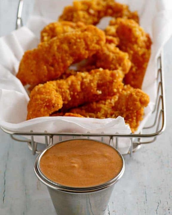 Homemade Red Robin Campfire Sauce in a ramekin in front of a basket of chicken tenders.