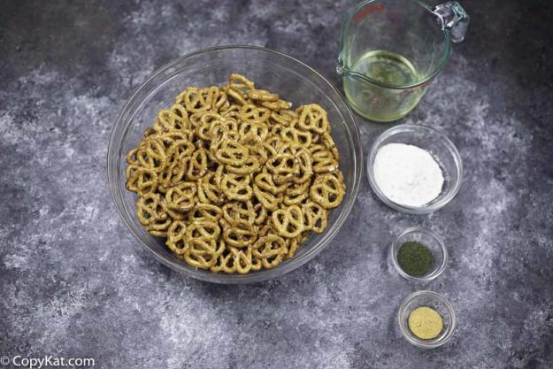 A bowl of pretzels, dry ranch salad dressing mix, garlic powder, vegetable oil, and dill weed.