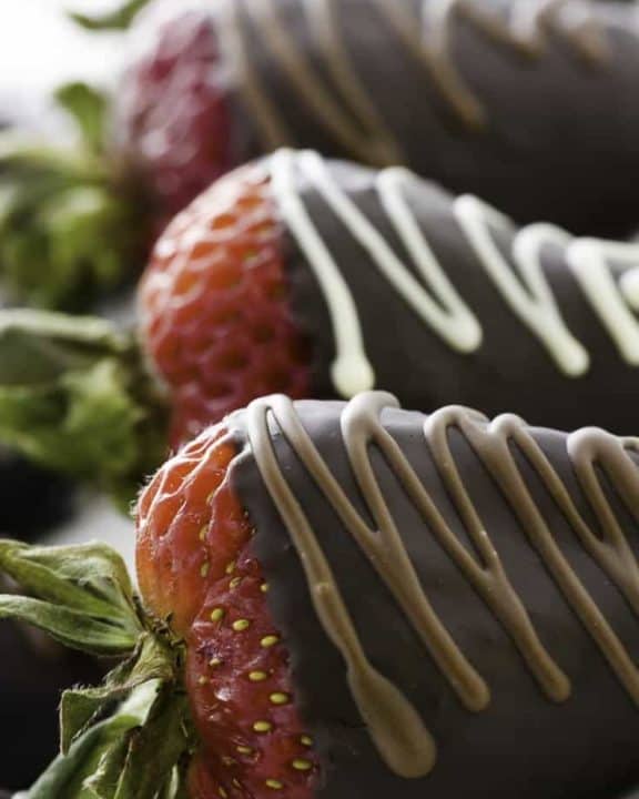 Three chocolate covered strawberries on a plate.