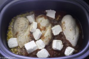 Adding cream cheese to the crockpot of chicken and black beans and corn