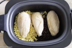 A crockpot with black beans, corn, and frozen chicken breasts.