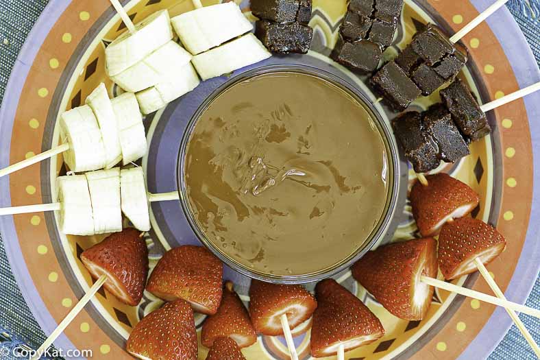 A fondue pot full of chocolate fondue with fruit skewers around it.