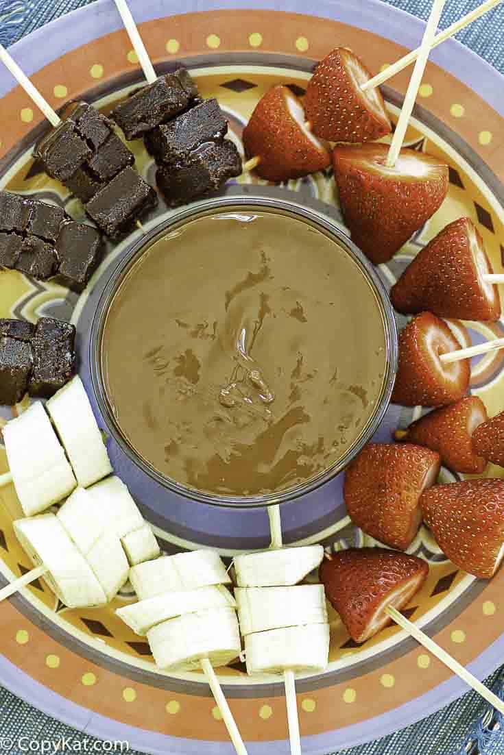 a bowl of chocolate fondue and fruit skewers on a platter.