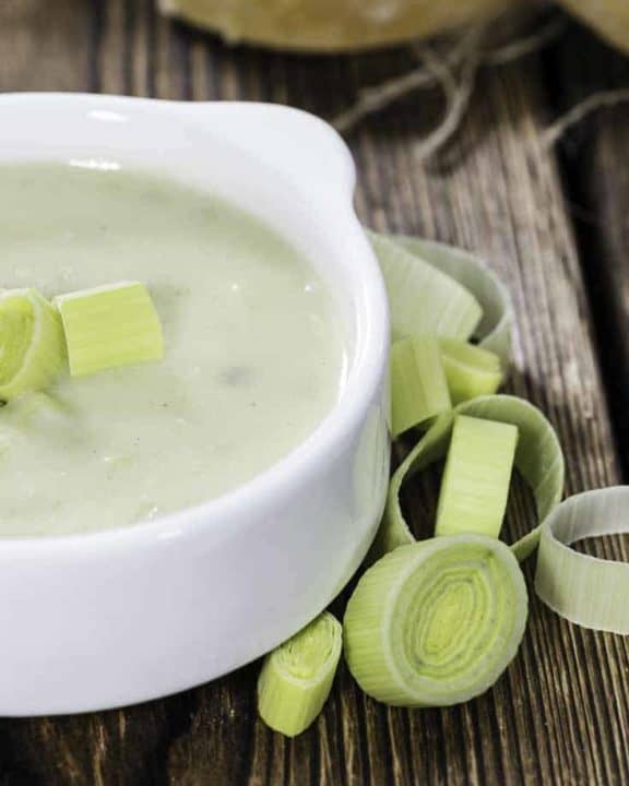 a bowl of potato leek soup with a few cut up leeks