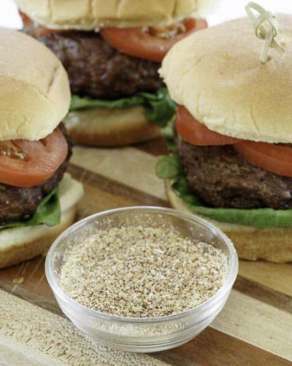 homemade burger seasoning and hamburgers on a wood cutting board.