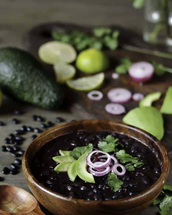 a bowl of cooked black beans with cilantro, lime, red onion and avocado.