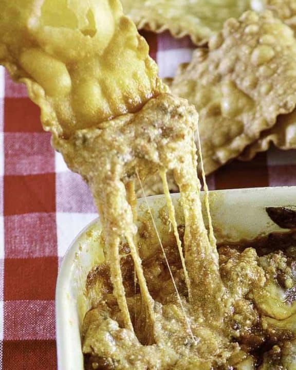 a pasta chip dipping into cheesy lasagna dip
