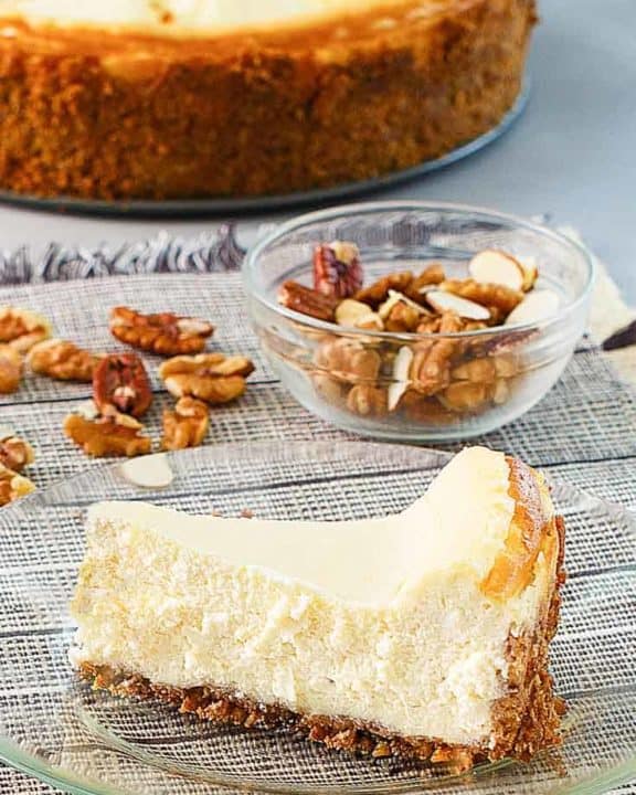 a slice of cheesecake, nuts, and a cheesecake on platter