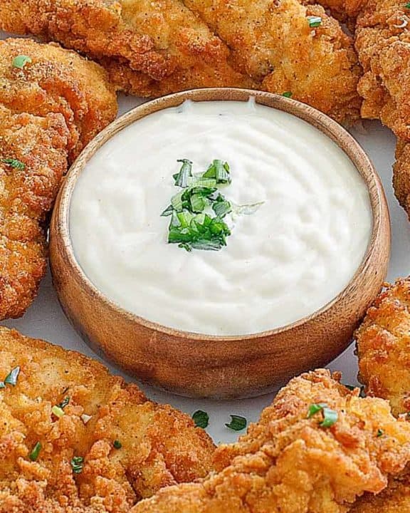 a bowl of Jan sauce with chicken tenders around it