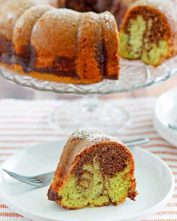 a slice of chocolate pistachio bundt cake in front of the cake on a stand