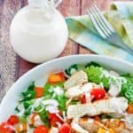 a bottle of creamy pesto dressing next to a salad with grilled chicken