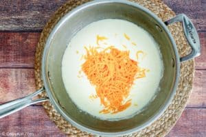 adding cheese to white sauce in a pan
