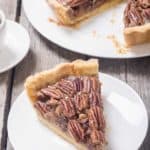 a slice of pecan pie on a white plate next to the pie