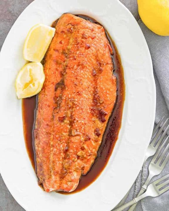 baked salmon with sauce and lemon wedges on a platter