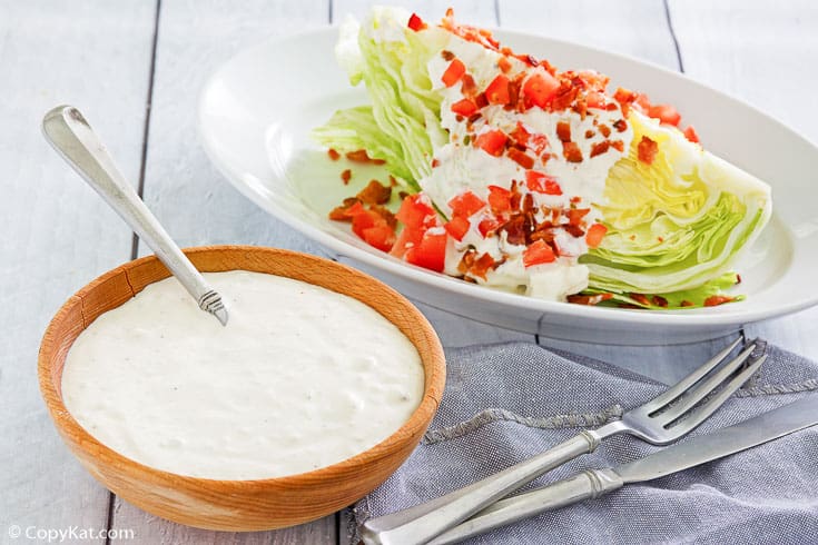 a bowl of homemade blue cheese dressing beside a wedge salad