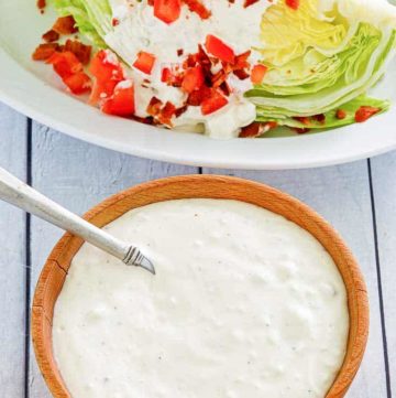 a bowl of blue cheese dressing next to a wedge salad