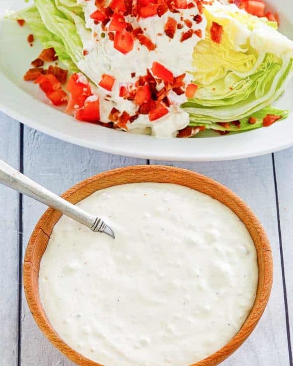 a bowl of blue cheese dressing next to a wedge salad