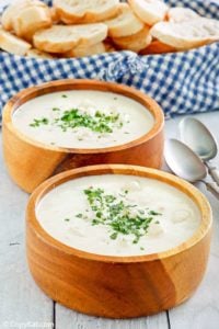 Two bowls of homemade Red Lobster clam chowder, two spoons, and a basket of bread slices