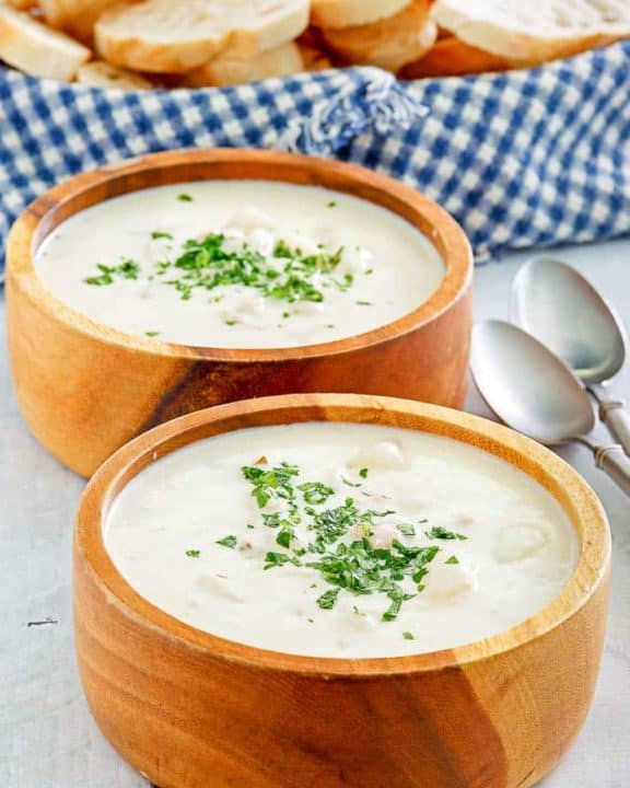 Two bowls of homemade Red Lobster clam chowder, two spoons, and a basket of bread slices