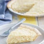 coconut cream pie slice on a plate with the pie on the table behind it