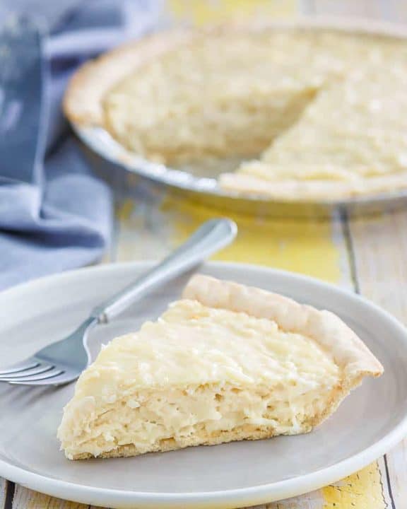 coconut cream pie slice on a plate with the pie on the table behind it