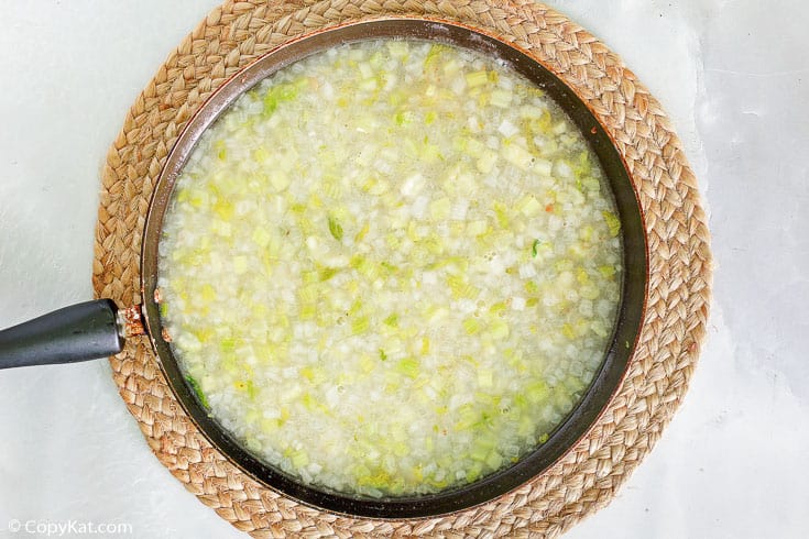 a skillet of vinegar dressing with onions and celery for hot German potato salad