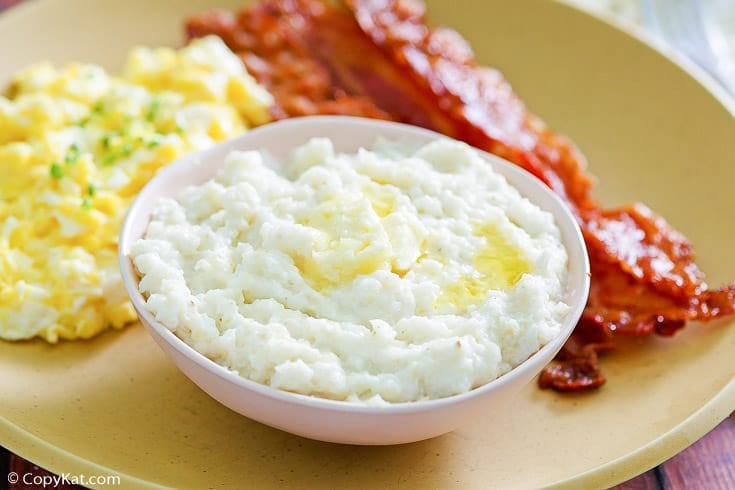 a bowl of homemade Luby's grits on a plate with eggs and bacon