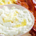 a bowl of grits, bacon and eggs on a plate