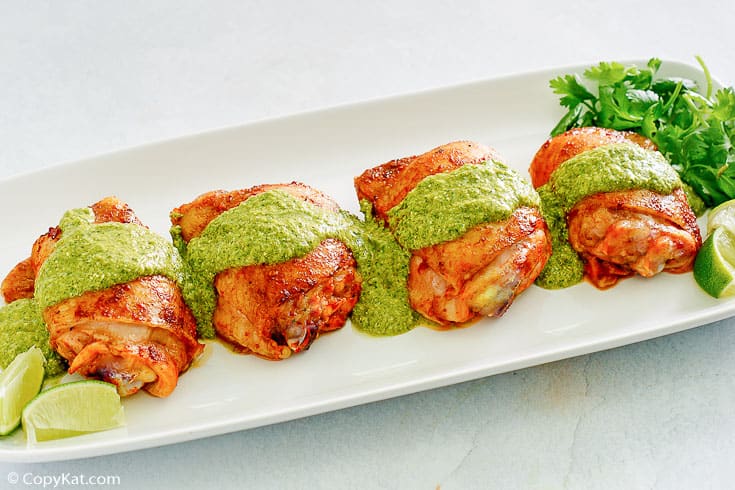 Peruvian chicken thighs topped with green sauce on a platter