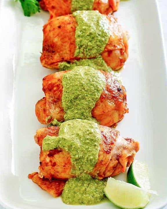 four Peruvian chicken thighs with green sauce on a platter