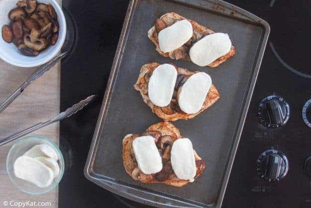 cooked chicken breasts topped with mushrooms and mozzarella cheese on a baking sheet