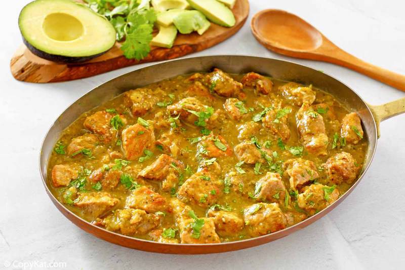 chili verde in a skillet, a wood spoon, and fresh avocado