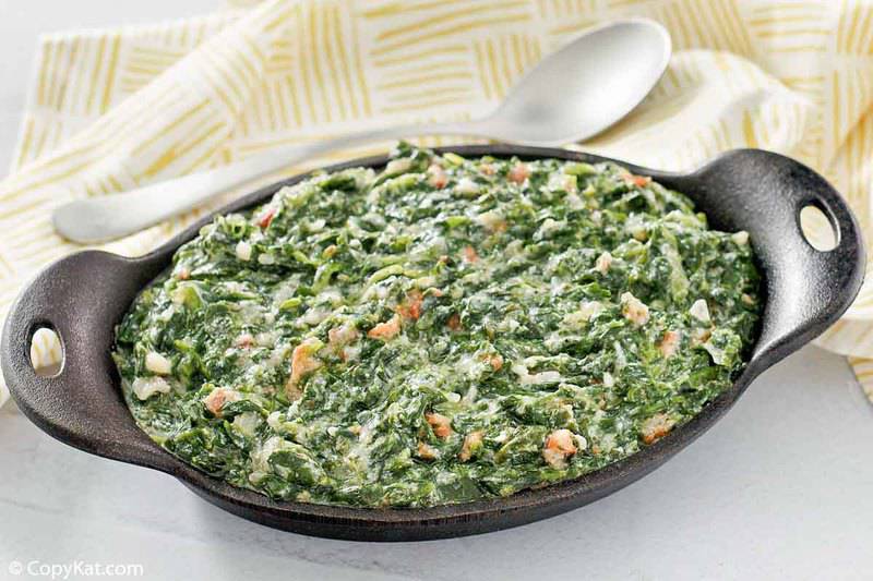 homemade Lawry's creamed spinach with bacon in a dish, a spoon, and cloth napkin