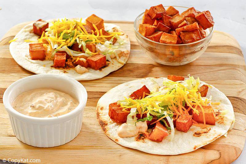 two homemade Taco Bell spicy potato tacos, a bowl of fried potatoes, and a bowl of chipotle sauce