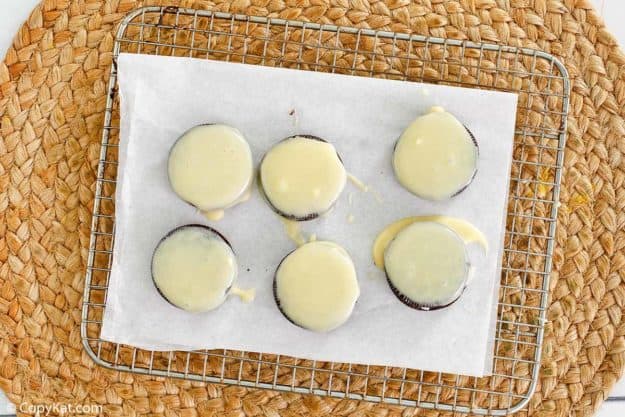 Oreos covered in white chocolate on a baking rack