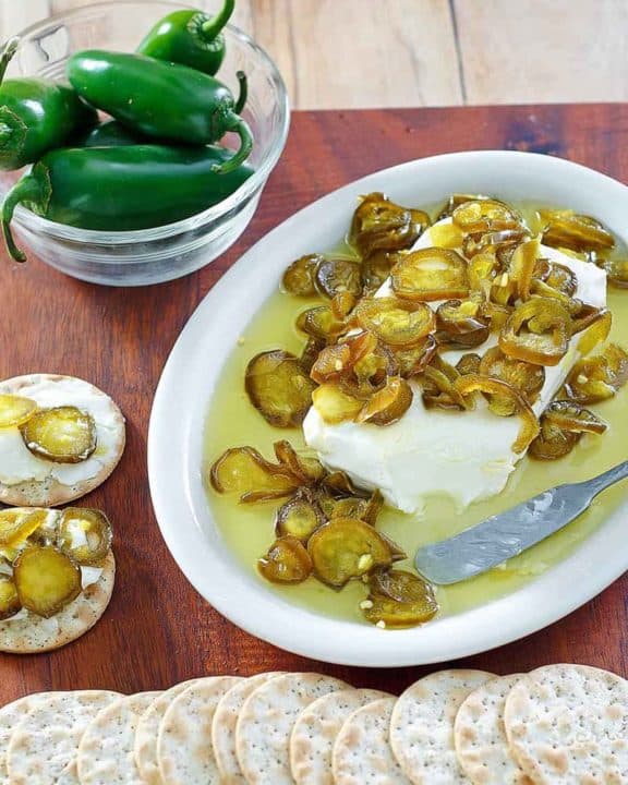 candied jalapenos over cream cheese on a platter next to crackers