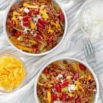 overhead view of bowls of Cincinnati chili, shredded cheese, chopped onions, and kidney beans