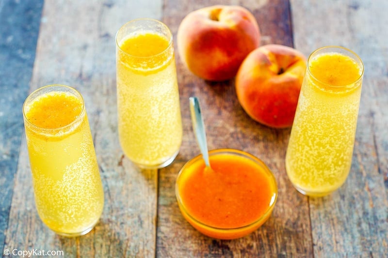 three homemade Harry's Bar Bellini drinks, two fresh peaches, and a bowl of peach puree