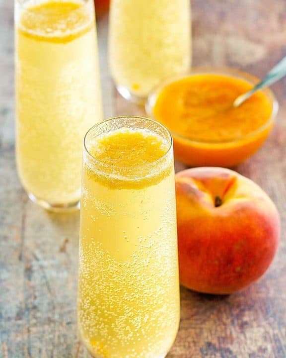 homemade Harry's Bar Bellini cocktails, a fresh peach, and peach puree