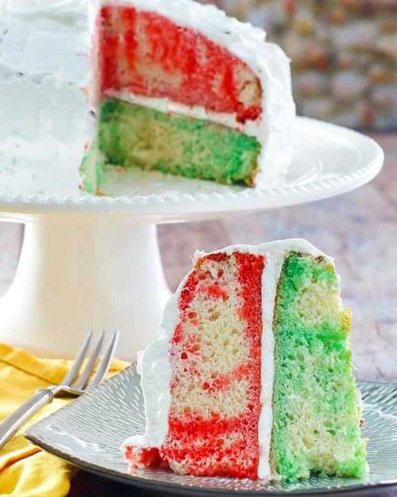 a slice of Jello poke cake in front the the cake on a stand