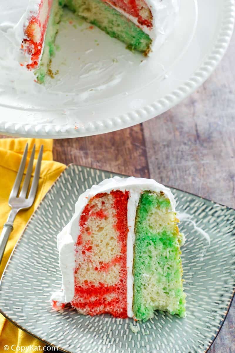 a slice of red and green Jello poke cake with Cool Whip frosting