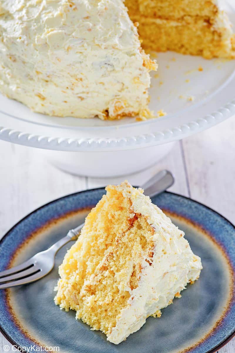 a slice of ambrosia cake on a plate in front of the cake on a stand