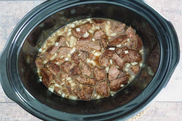 browned beef tips, onions, and stock in a slow cooker