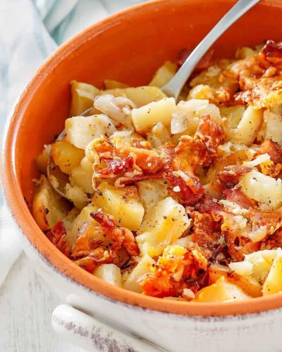 Crockpot cheesy potatoes with bacon and a spoon in a bowl